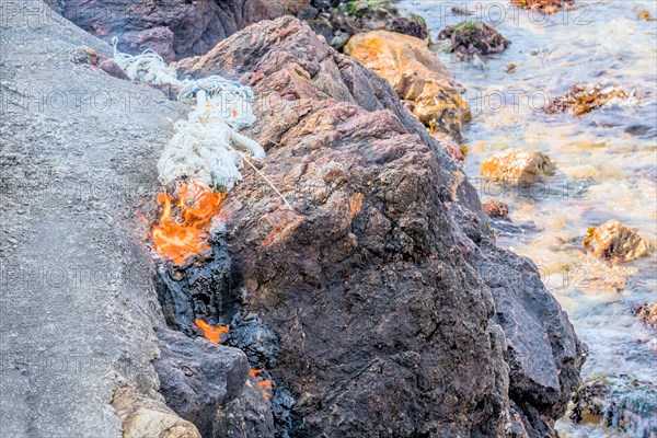 Marine rope burning on top of large boulder on coast of seaport in South Korea