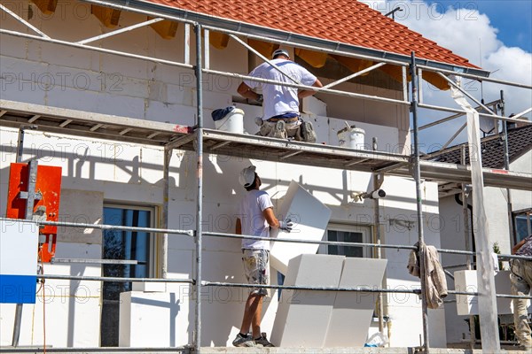 Construction workers insulate a house facade