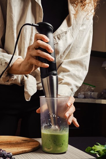 Unrecognizable woman using blender in the kitchen to make banana and spinach smoothie