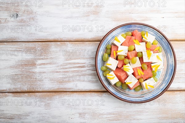 Vegetarian salad with watermelon, feta cheese, and grapes on blue ceramic plate on white wooden background. top view, copy space, flat lay