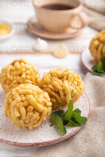 Traditional Tatar candy chak-chak made of dough and honey with cup of coffee on a white wooden background and linen textile. Side view, close up, selective focus