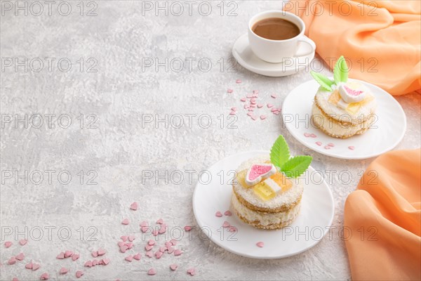 Decorated cake with milk and coconut cream with cup of coffee on a gray concrete background and orange textile. Side view, copy space