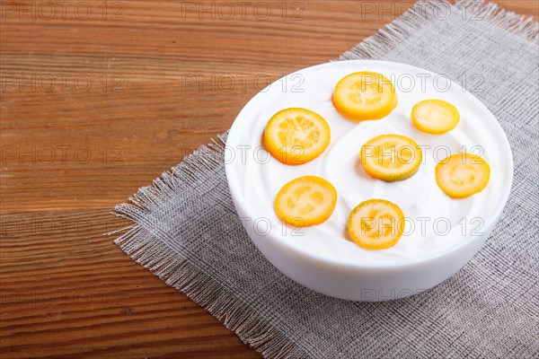 Greek yogurt with kumquat pieces in a white plate on a brown wooden background, close up