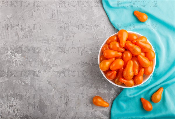 Fresh orange grape tomatoes in white ceramic bowl on gray concrete background with blue textile. top view, flat lay, copy space