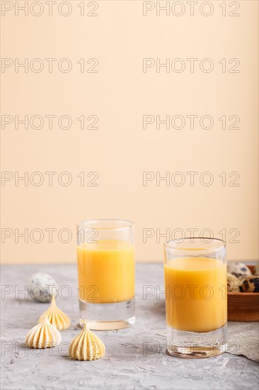 Sweet egg liqueur in glass with quail eggs and meringues on a gray and orange background. Side view, copy space