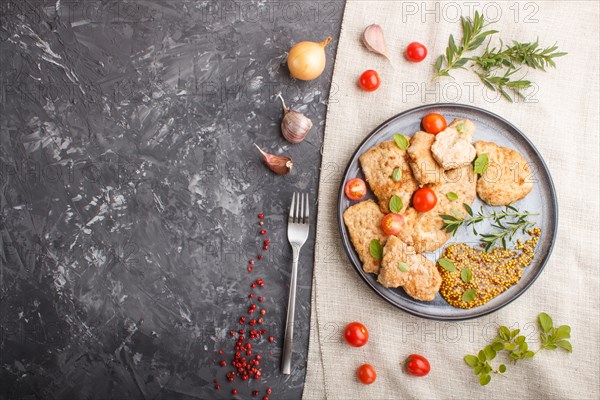 Fried pork chops with tomatoes and herbs on a gray ceramic plate on a black concrete background and linen textile. top view, flat lay, copy space