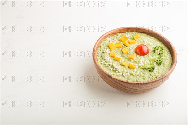 Green broccoli cream soup in wooden bowl on a white wooden background. side view, copy space
