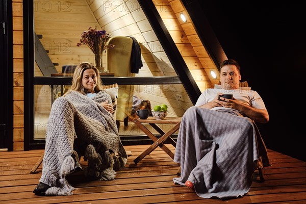 In the evening, a couple sits on the terrace of their wooden cabin and talks