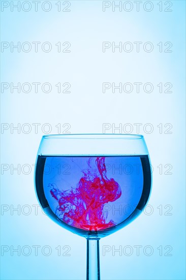 Red colour mixes with water in a glass against a blue background, Abstract
