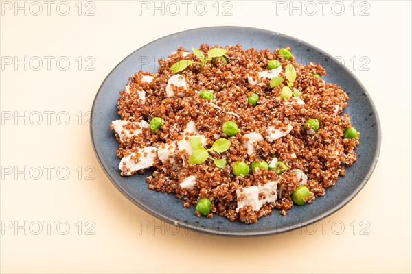 Quinoa porridge with green pea and chicken on ceramic plate on a pastel orange background. Side view, close up