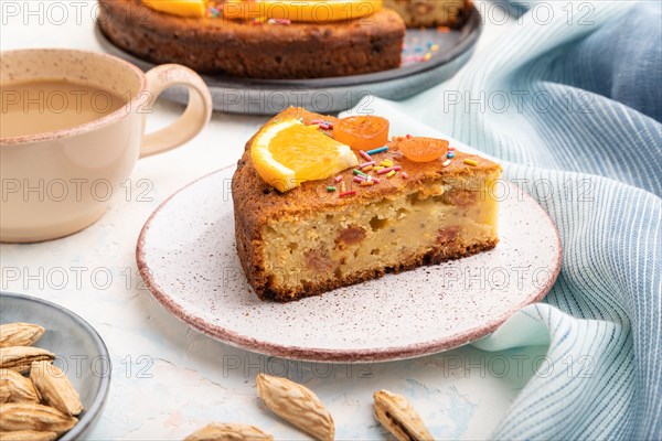 Orange cake with almonds and a cup of coffee on a white concrete background and blue linen textile. Top view, close up