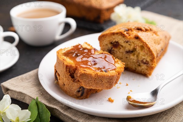 Homemade cake with raisins, almonds, soft caramel and a cup of coffee on a black concrete background and linen textile. Side view, close up, selective focus