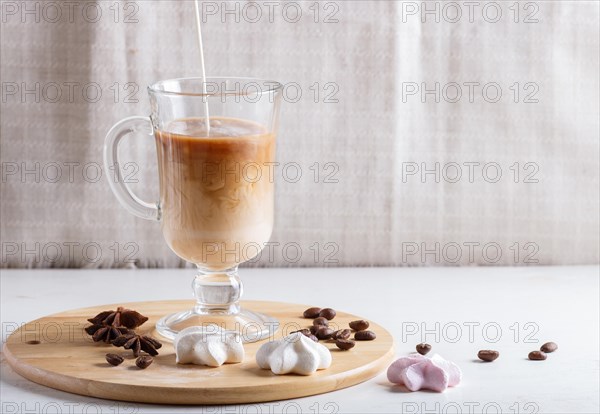 Glass cup of coffee with cream poured over and meringues on a wooden board on a white background. close up, copy space