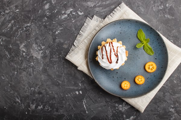 Cake with whipped egg cream on a blue ceramic plate with kumquat slices and mint leaves on a black concrete background with linen napkin. copy space, flat lay, top view