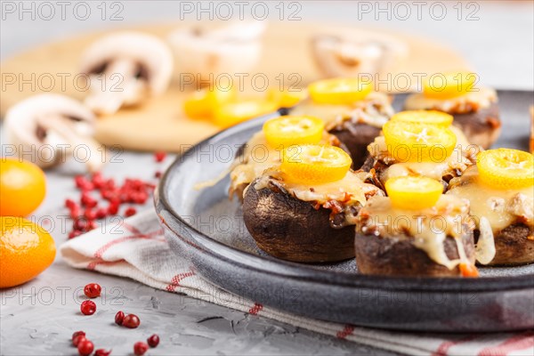 Stuffed fried champignons with cheese, kumquats and green peas on a gray concrete background. ceramic plate, side view, close up, selective focus