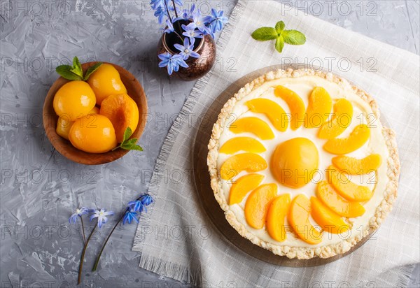 Round peach cheesecake and ceramic vase with blue flowers on a linen napkin on a gray concrete background. top view, close up