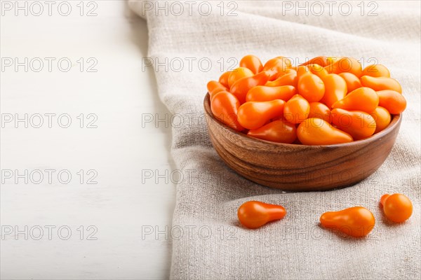 Fresh orange grape tomatoes in wooden bowl on white wooden background with linen napkin. side view, close up, copy space