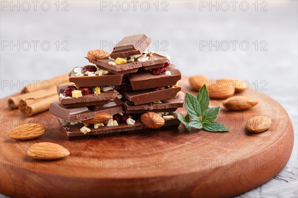 A pieces of milk chocolate with almonds and dried fruits on a brown wooden board on a gray concrete background. side view, close up, selective focus