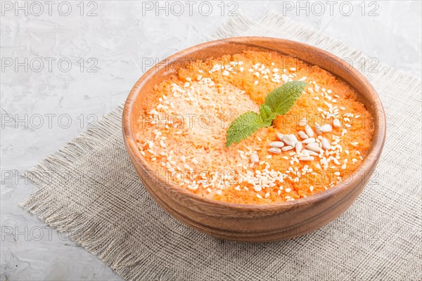 Carrot cream soup with sesame seeds in wooden bowl on a gray concrete background with linen textile. side view, close up