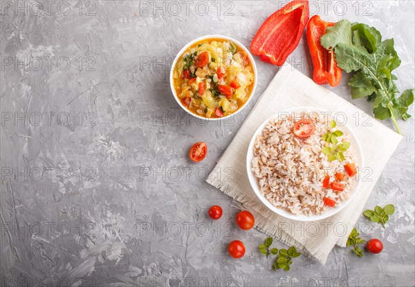 Unpolished rice porridge with stewed vegetables and oregano in white bowl on a gray concrete background and linen textile. Top view, flat lay, copy space