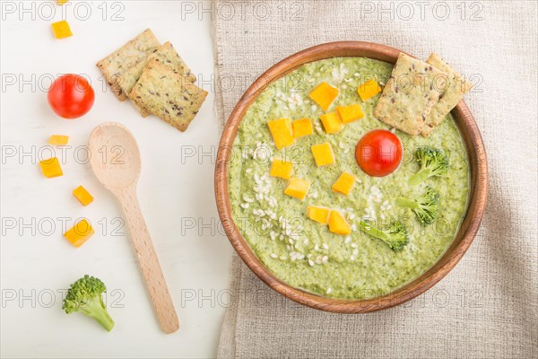 Green broccoli cream soup with crackers and cheese in wooden bowl on a white wooden background and linen napkin. top view, flat lay, close up