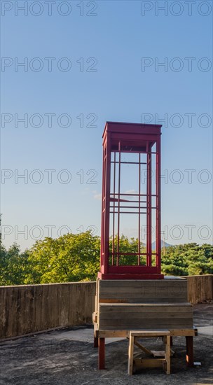 Red wooden telephone booth minus phone and without glass on roof of building on sunny day with blue skies in South Korea
