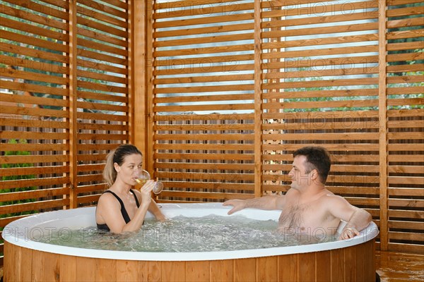 Beautiful couple in love relaxing and drinking wine in outdoor hot tub during weekend