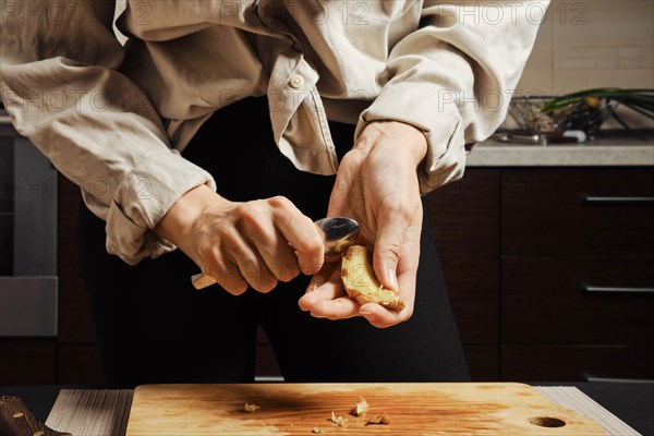 Female hands peeling ginger with spoon in the kitchen