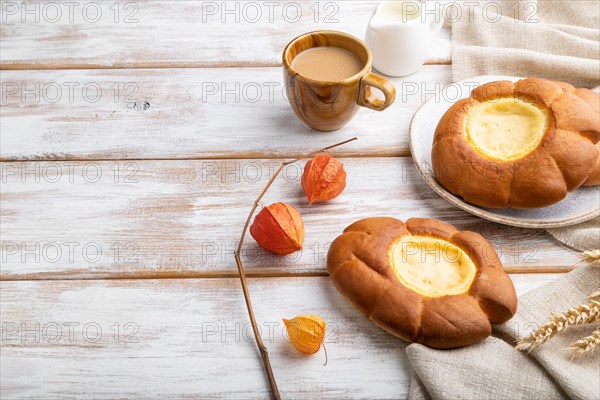 Sour cream bun with cup of coffee on a white wooden background and linen textile. Side view, copy space