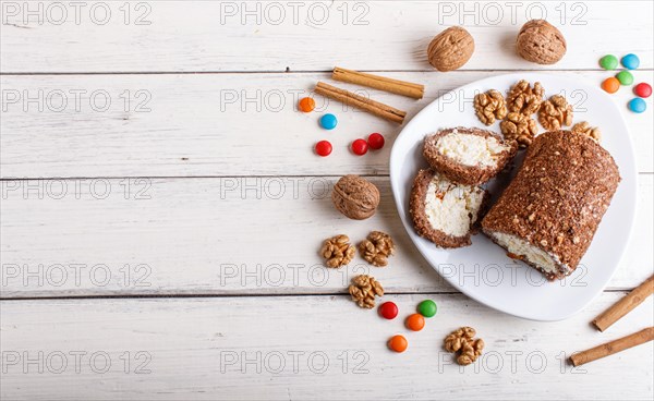 Roll cake with curd and walnuts isolated on white wooden background. top view, copy space