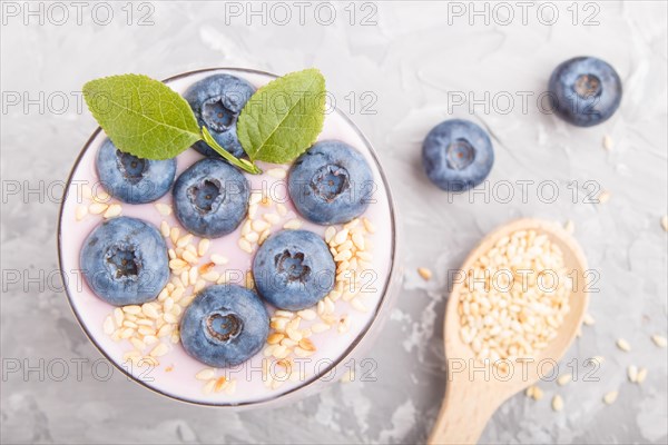 Yoghurt with blueberry and sesame in a glass and wooden spoon on gray concrete background. top view, flat lay, close up