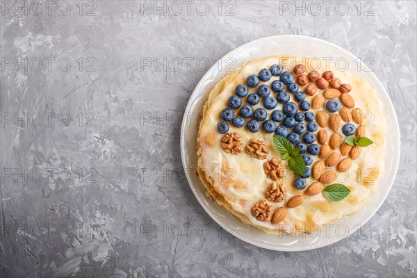 Homemade layered Napoleon cake with milk cream. Decorated with blueberry, almonds, walnuts, hazelnuts, mint on a gray concrete background. top view. flat lay, copy space