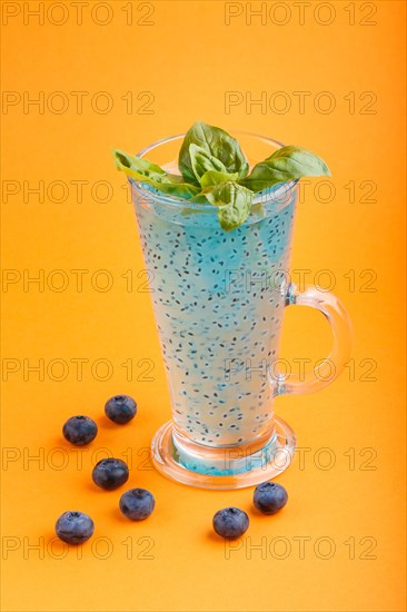 Glass of blueberry blue colored drink with basil seeds on orange background. Morninig, spring, healthy drink concept. Side view, selective focus, close up