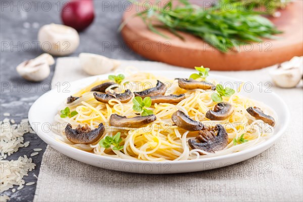 Rice noodles with champignons mushrooms, egg sauce and oregano on white ceramic plate on a black concrete background. side view, selective focus, close up