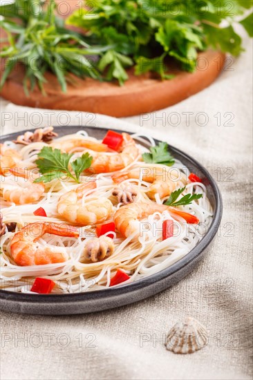 Rice noodles with shrimps or prawns and small octopuses on gray ceramic plate on a white linen textile. side view, close up, selective focus