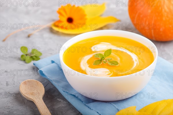Traditional pumpkin cream soup with in white bowl on a gray concrete background with blue napkin. side view, close up, selective focus