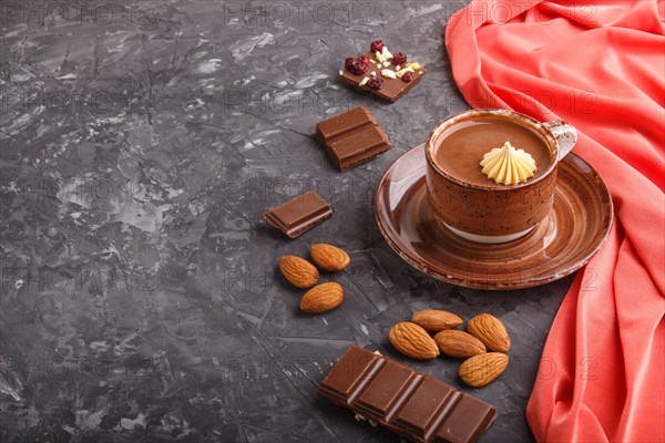 Cup of hot chocolate and pieces of milk chocolate with almonds on a black concrete background with red textile. side view, copy space