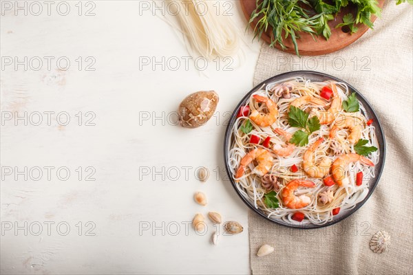 Rice noodles with shrimps or prawns and small octopuses on gray ceramic plate on a white wooden background and linen textile. Top view, flat lay, copy space