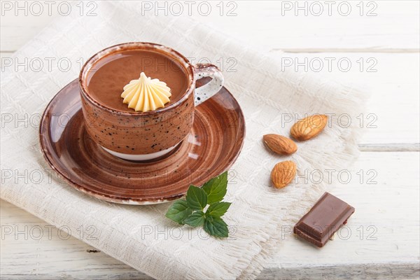 Cup of hot chocolate and pieces of milk chocolate with almonds on a white wooden background with linen napkin. side view, close up