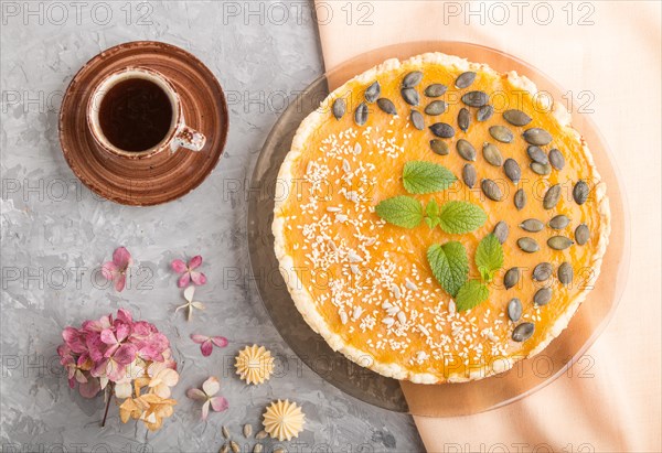 Traditional american sweet pumpkin pie decorated with mint, sesame and pumpkin seeds with cup of coffee on a gray concrete background. top view, flat lay, close up