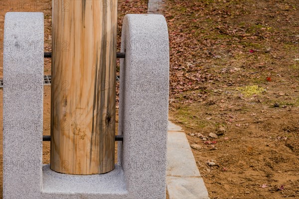 Closeup of bottom of unpainted wooden post held in concrete footing with large threaded bolts in South Korea