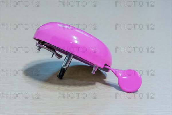 Pink handlebar bicycle bell with top missing isolated on light wood grain background