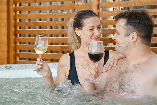Happy couple looking at each other while relaxing in hot tub and drinking wine