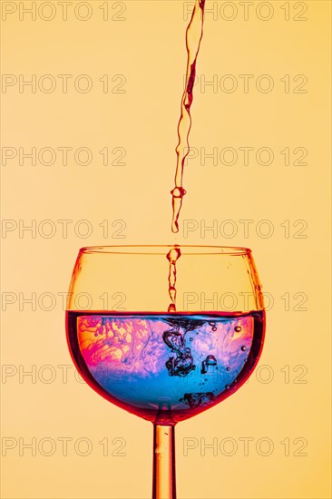 Colourful liquids meet in a wine glass, creating a sense of movement, yellow background