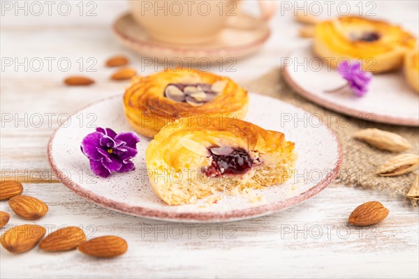 Small cheesecakes with jam and almonds with cup of coffee on a white wooden background and linen textile. Side view, close up, selective focus