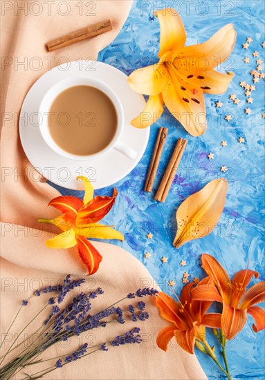 Orange day-lily and lavender flowers and a cup of coffee on a blue concrete background, with orange textile. Morninig, spring, fashion composition. Flat lay, top view, close up