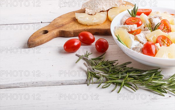 Chicken fillet salad with rosemary, pineapple and cherry tomatoes on white wooden background. close up