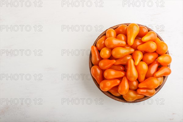 Fresh orange grape tomatoes in wooden bowl on white wooden background. top view, flat lay, copy space