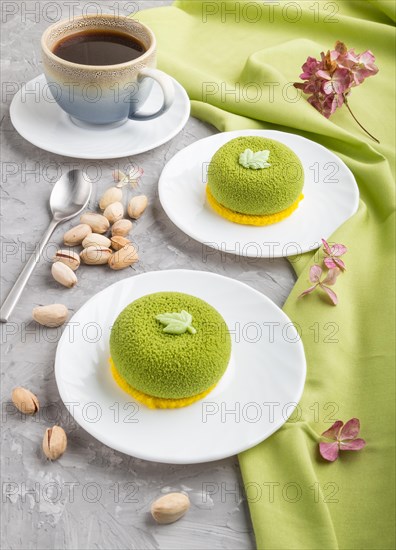 Green mousse cake with pistachio cream and a cup of coffee on a gray concrete background and green textile. side view, close up