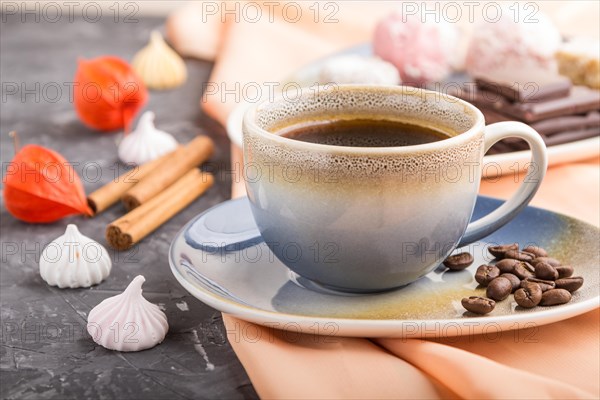 A cup of coffee with chocolate and coconut candies on a black concrete background and orange textile. side view, close up, selective focus